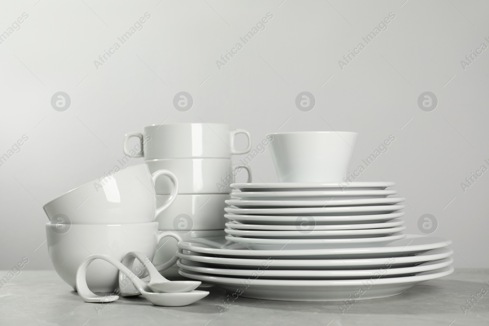 Photo of Set of clean dishware on grey table against light background