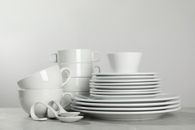 Set of clean dishware on grey table against light background