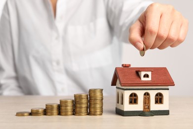 Photo of Mortgage concept. Woman putting coin into house model at wooden table, closeup