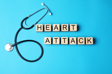 Photo of Wooden cubes with words HEART ATTACK and stethoscope on color background, top view