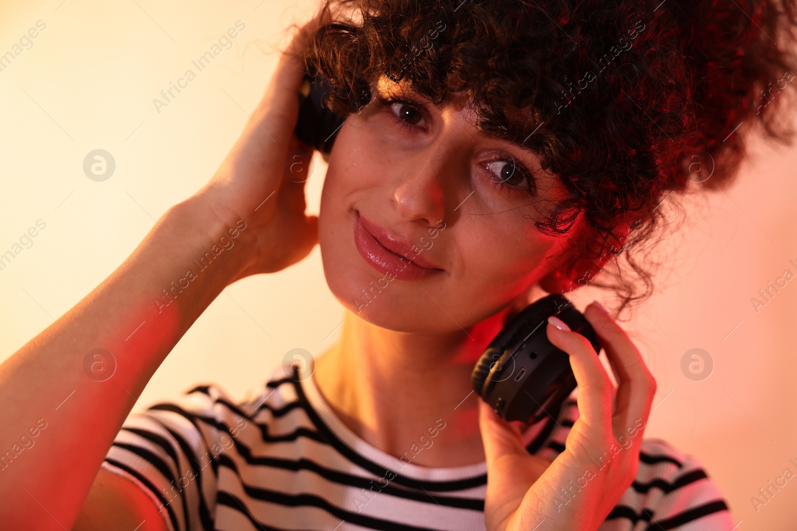 Photo of Beautiful young woman listening to music with headphones on color background in neon lights, closeup