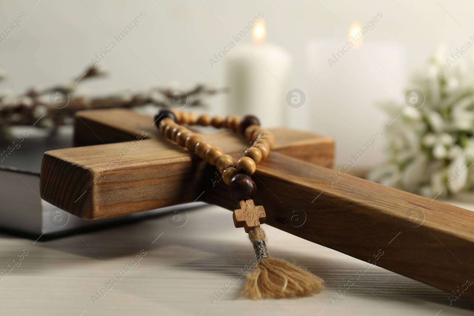 Photo of Wooden cross and rosary beads on white table, closeup