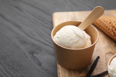 Photo of Paper cup with delicious ice cream and vanilla pods on grey wooden table, closeup. Space for text