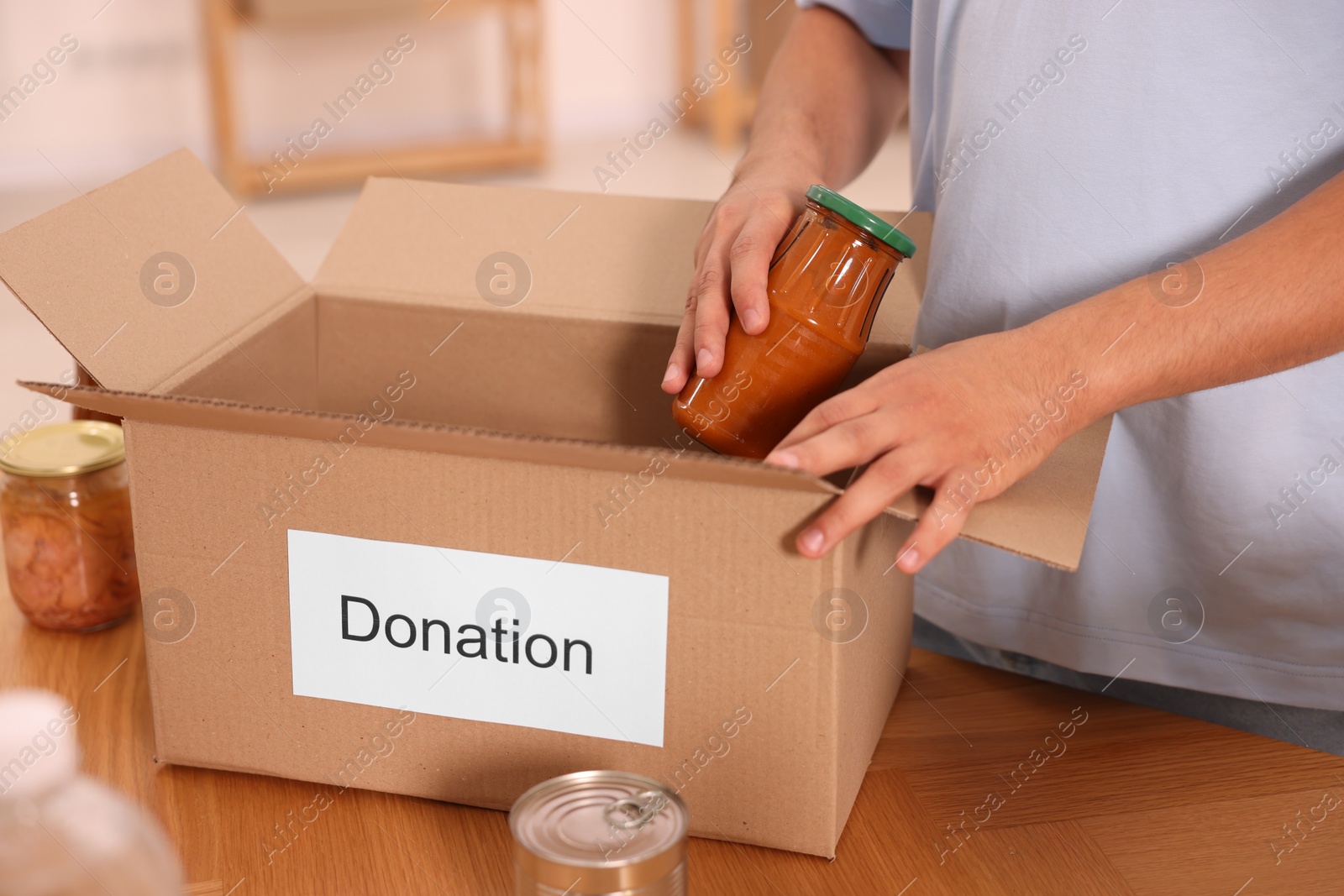 Photo of Volunteer packing food products at table indoors, closeup