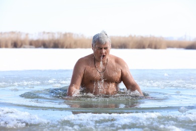Photo of Mature man immersing in river on winter day. Baptism ritual