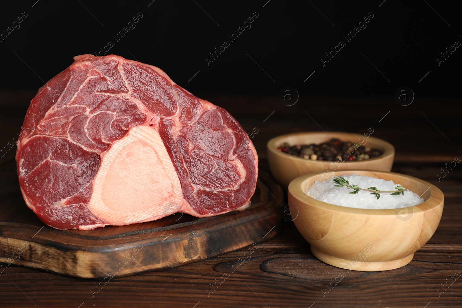 Photo of Piece of raw beef meat and spices on wooden table against black background, closeup