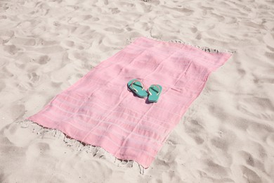 Pink striped beach towel and flip flops on sand