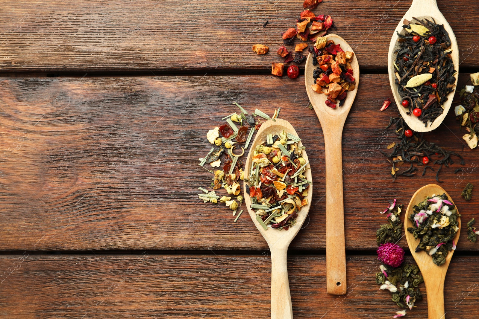 Photo of Flat composition with spoons of dried herbal tea leaves on wooden table. Space for text