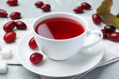 Photo of Cup of fresh dogwood tea and berries on light grey table