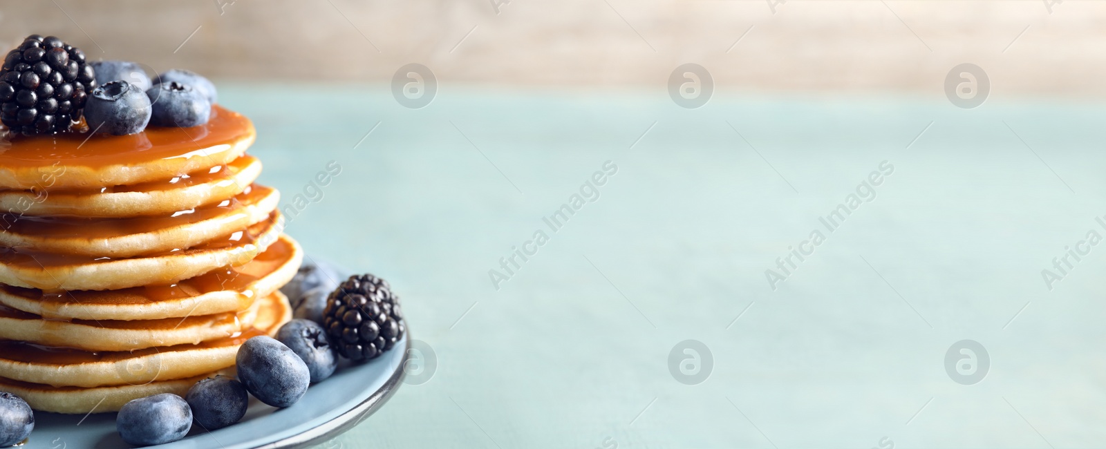 Image of Tasty pancakes with berries and syrup on plate, space for text. Banner design