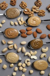 Photo of Tasty nut butters in spoons and raw nuts on gray table, flat lay