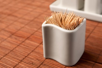 Photo of Holder with many toothpicks on bamboo mat, closeup. Space for text