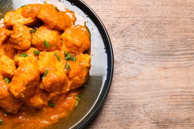 Photo of Plate of delicious chicken curry on wooden table, top view. Space for text