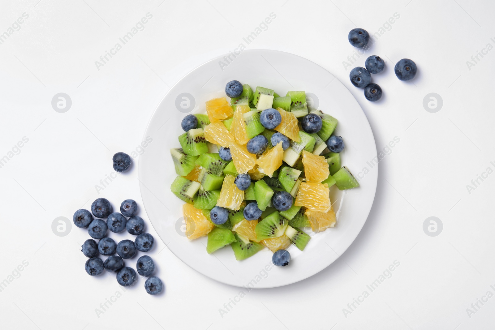 Photo of Plate of tasty fruit salad and blueberries on white background, flat lay