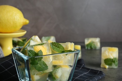 Photo of Ice cubes with mint and lemon in bowl on table. Space for text