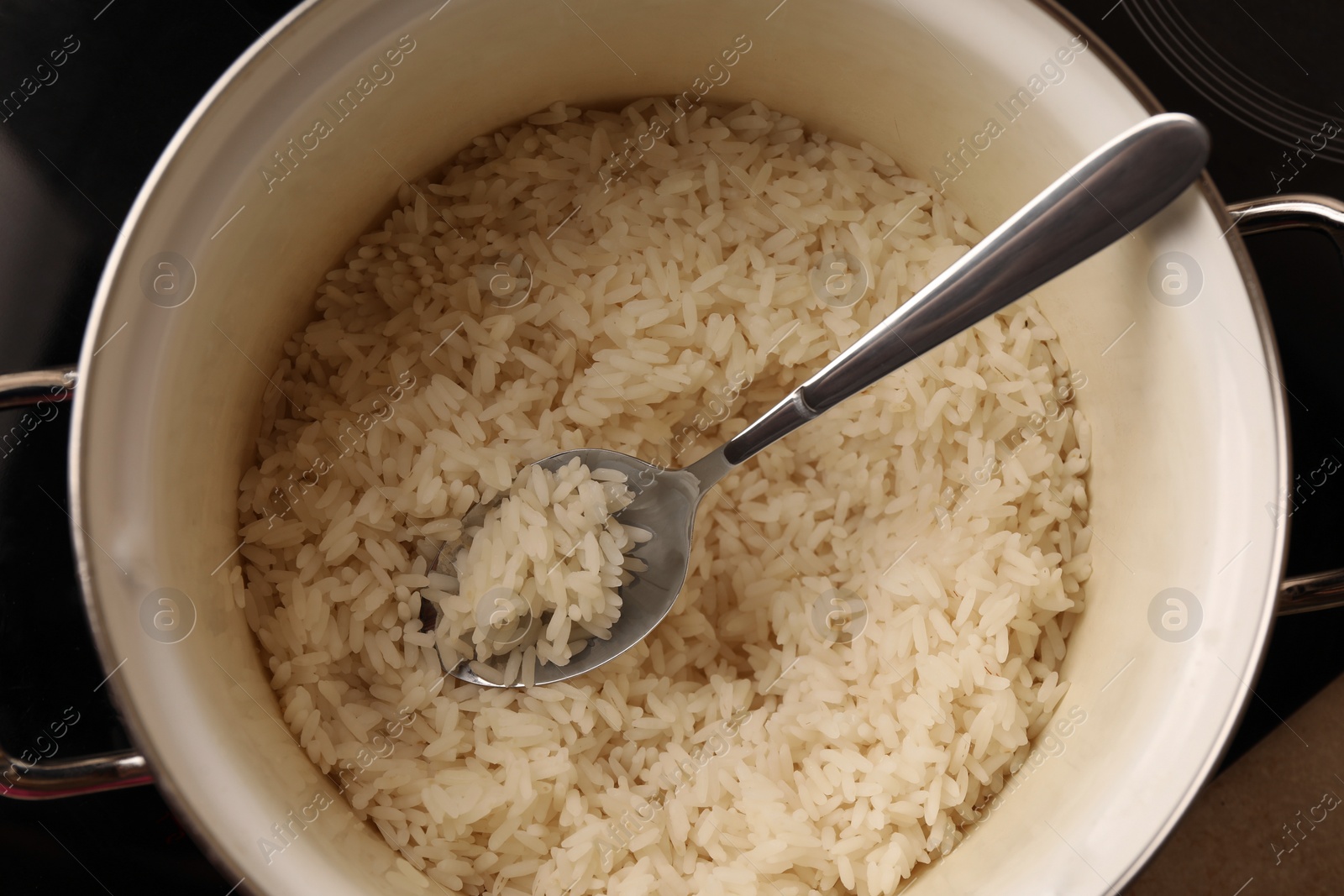 Photo of Pot with delicious rice and spoon on stove, top view