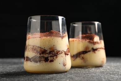 Photo of Delicious tiramisu in glasses on grey textured table, closeup