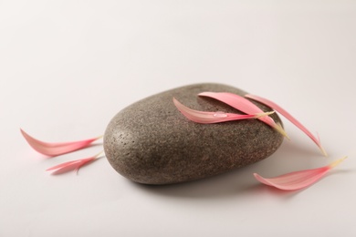 Spa stone with flower petals on light background