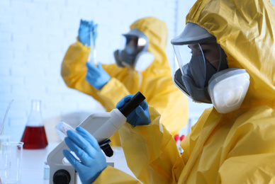 Scientist in chemical protective suit using microscope at laboratory, closeup. Virus research