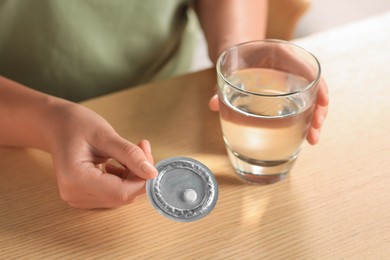 Photo of Woman taking emergency contraception pill at wooden table indoors, closeup