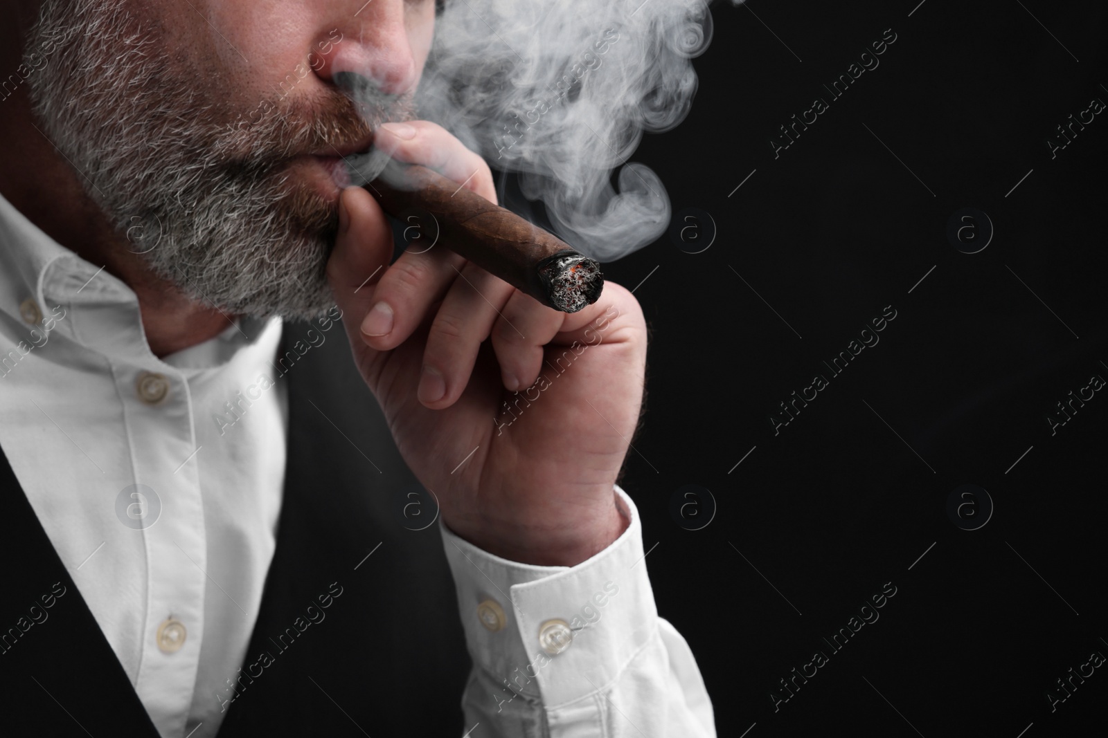 Photo of Bearded man smoking cigar against black background, closeup. Space for text