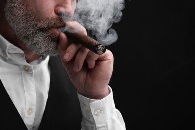 Photo of Bearded man smoking cigar against black background, closeup. Space for text