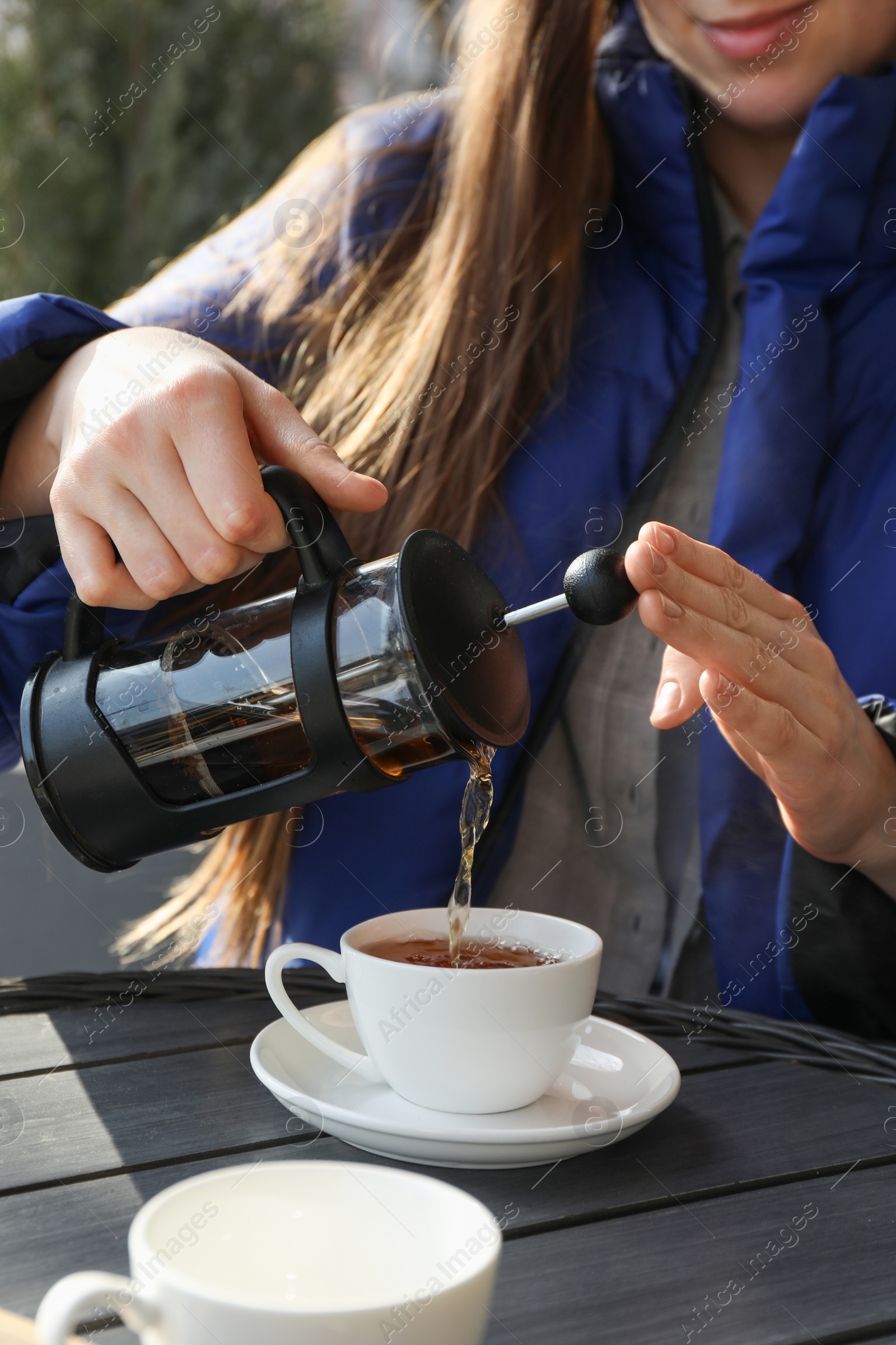 Photo of Woman pouring tea into cup at black wooden table in outdoor cafe, closeup