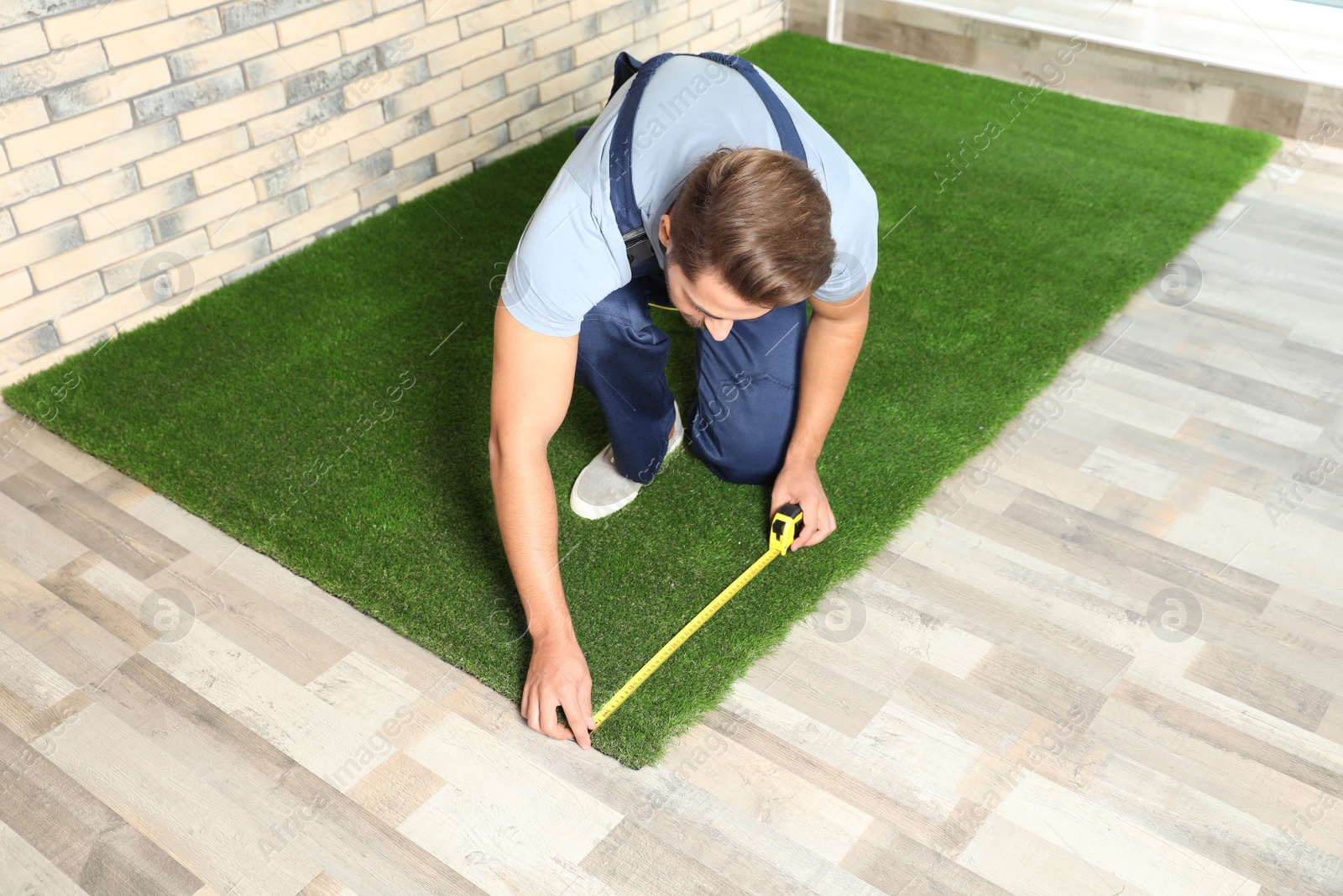 Photo of Man measuring artificial grass carpet indoors. Space for text