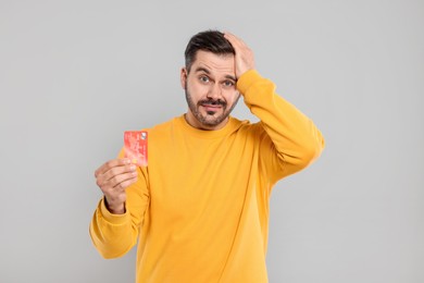 Photo of Confused man with credit card on grey background. Debt problem