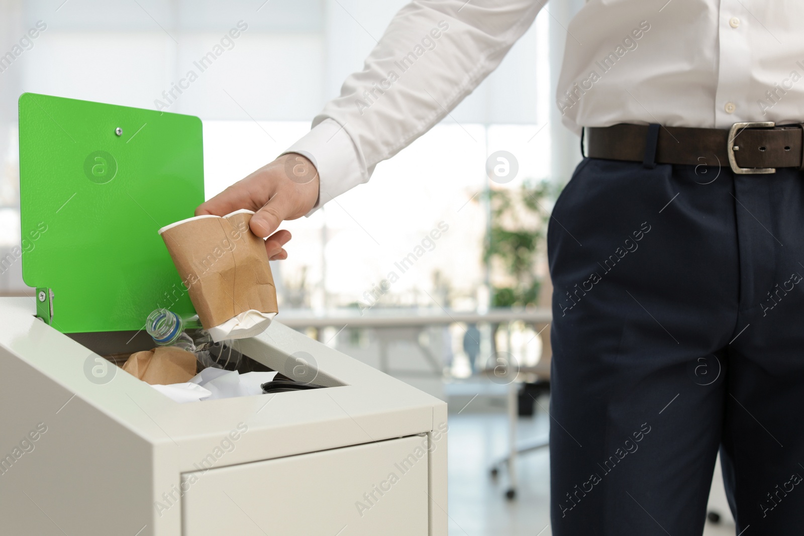 Photo of Man putting used paper cup into trash bin in office, closeup. Waste recycling