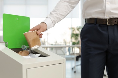 Man putting used paper cup into trash bin in office, closeup. Waste recycling