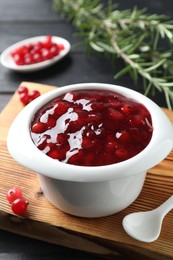 Photo of Cranberry sauce in bowl, fresh berries, spoon and rosemary on table, closeup