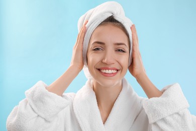 Beautiful young woman with hair wrapped in towel after washing on light blue background