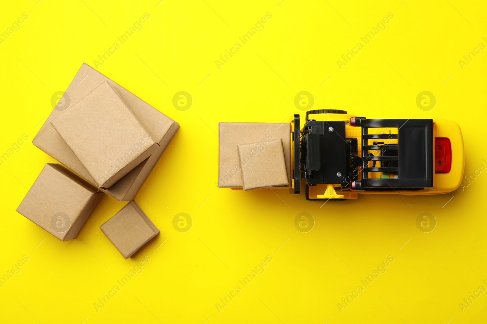 Photo of Top view of toy forklift with boxes on yellow background. Logistics and wholesale concept