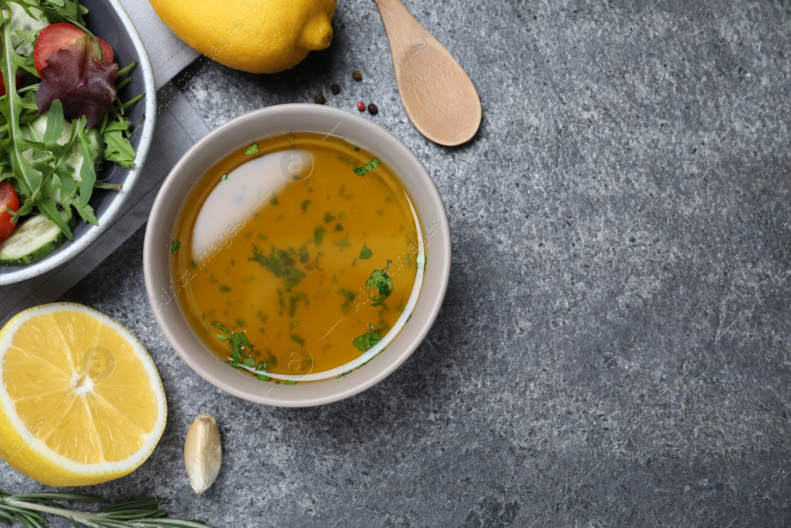 Photo of Bowl with lemon dressing near salad on grey table, flat lay with space for text. Delicious salad dressing