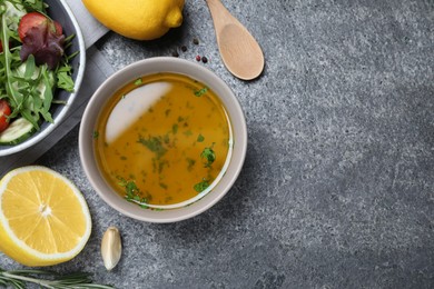 Bowl with lemon dressing near salad on grey table, flat lay with space for text. Delicious salad dressing