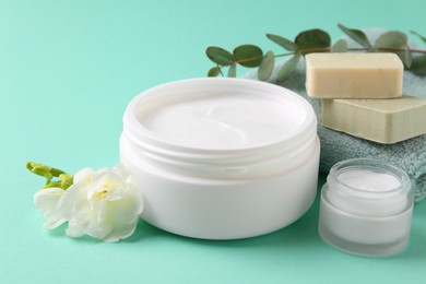 Photo of Moisturizing cream in open jars, soap bars and freesia flower on turquoise background. Body care products