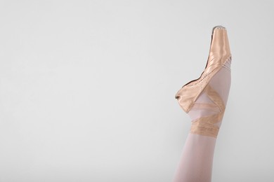 Young ballerina in pointe shoes practicing dance moves on light grey background, closeup. Space for text