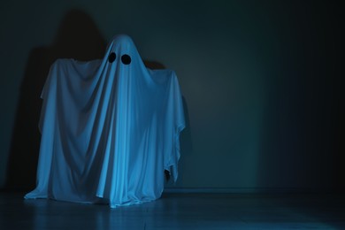 Photo of Creepy ghost. Woman covered with sheet in color light, space for text