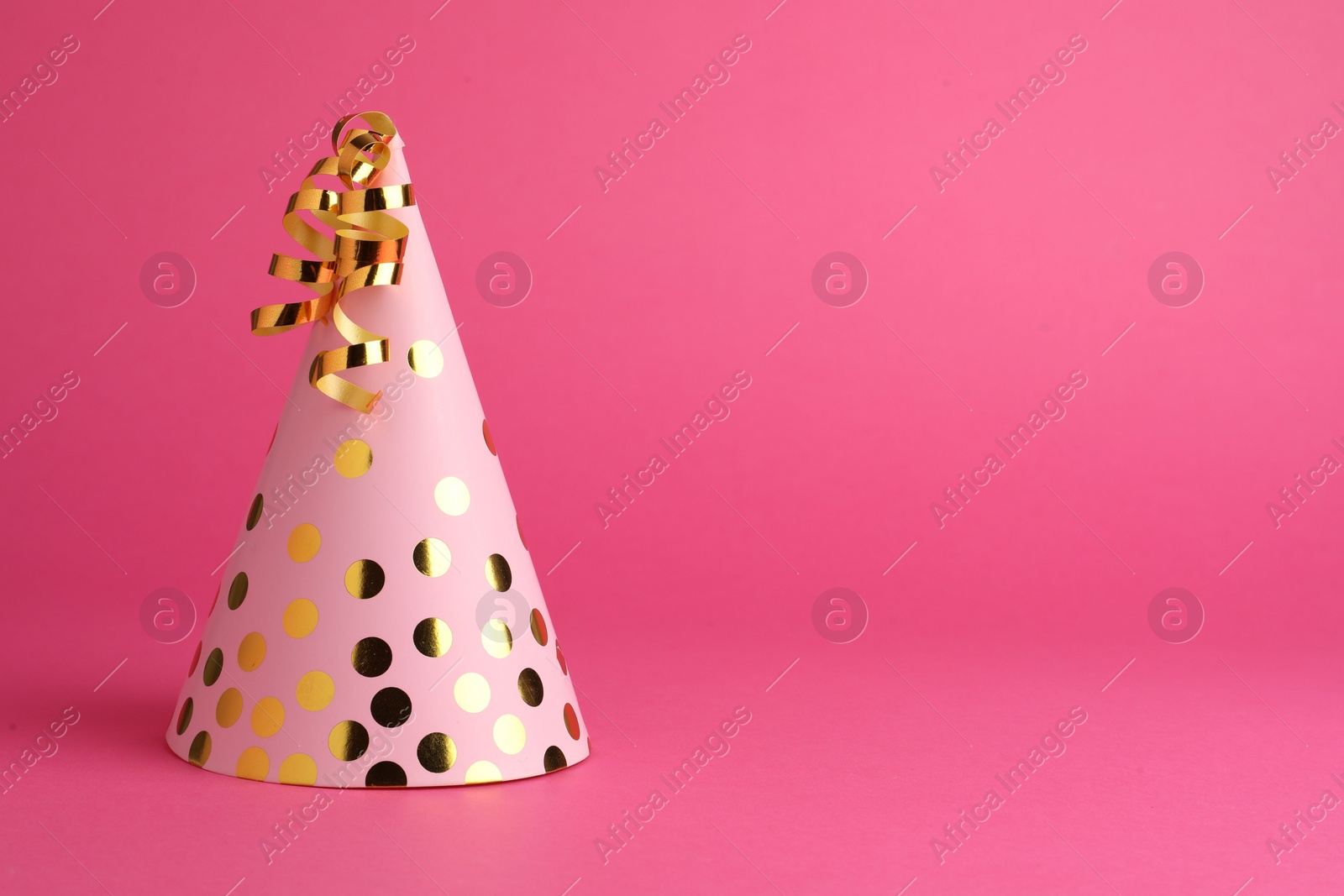 Photo of One beautiful party hat with serpentine streamers on pink background. Space for text