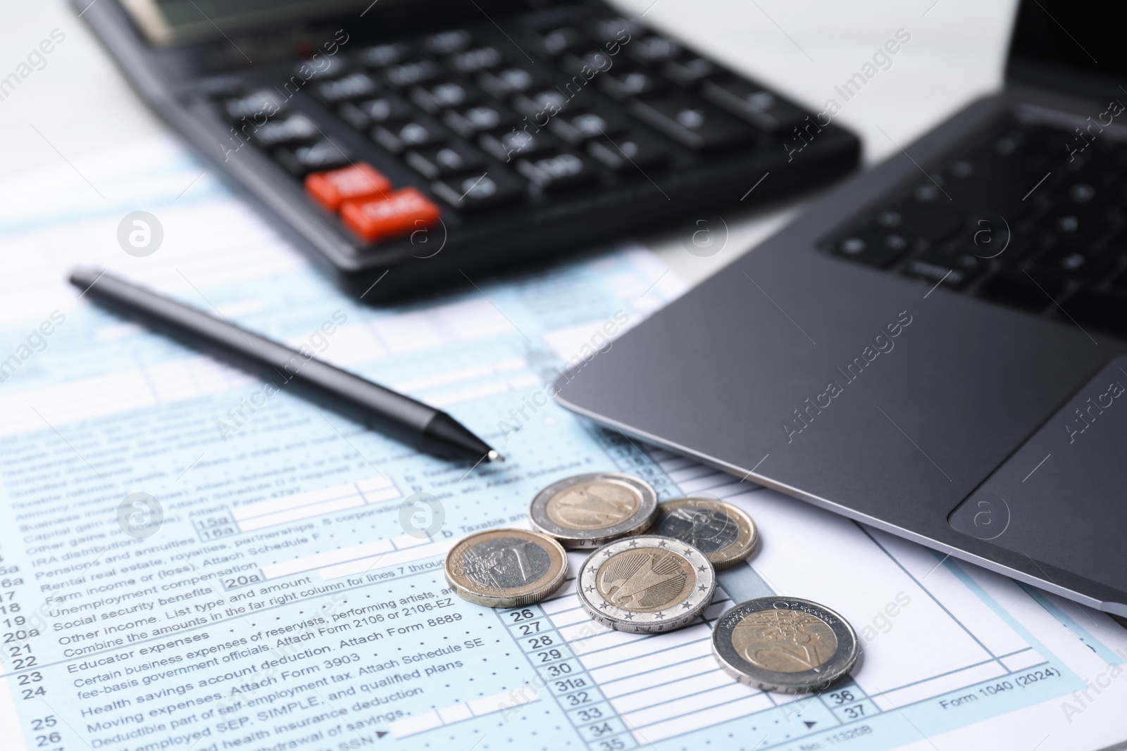 Photo of Tax forms, coins, pen, calculator and laptop on table, closeup