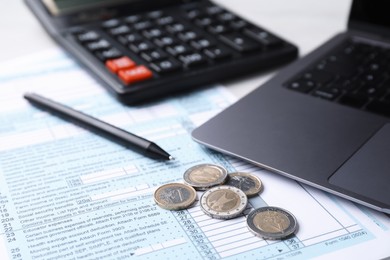 Tax forms, coins, pen, calculator and laptop on table, closeup