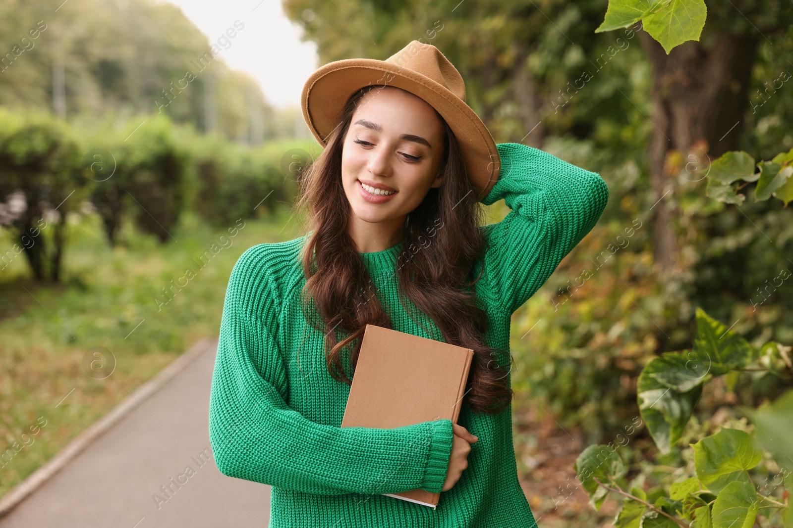Photo of Beautiful young woman in stylish warm sweater with book outdoors