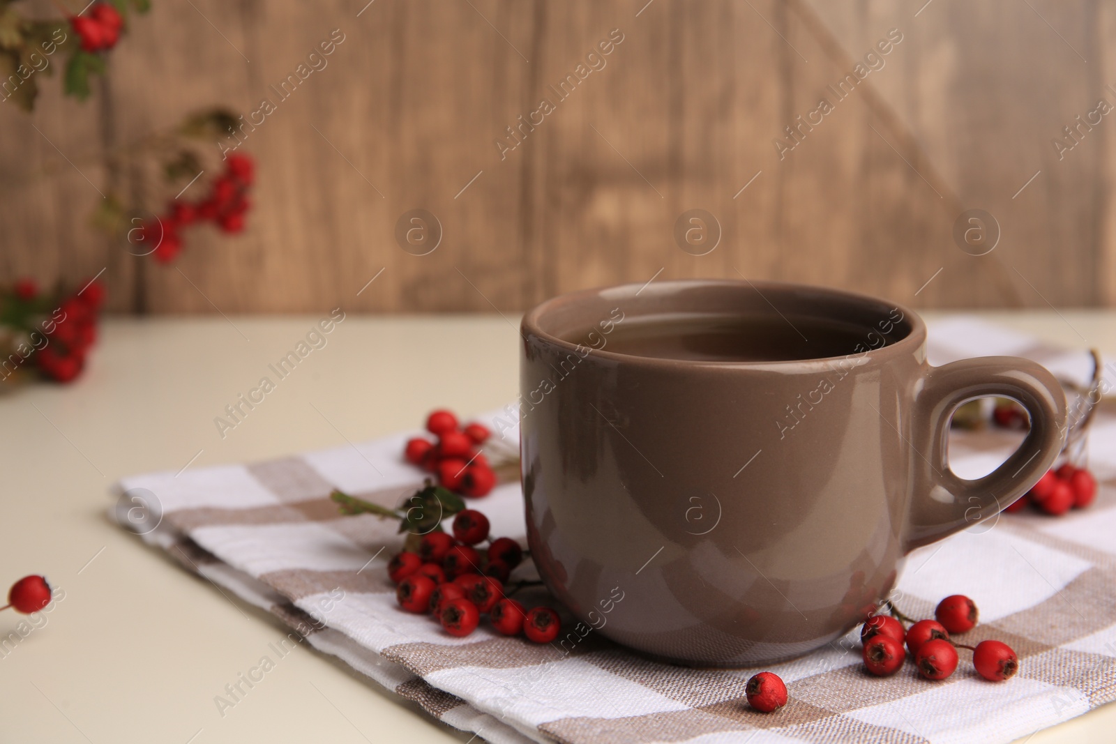 Photo of Brown cup with hawthorn tea and berries on beige table, closeup. Space for text