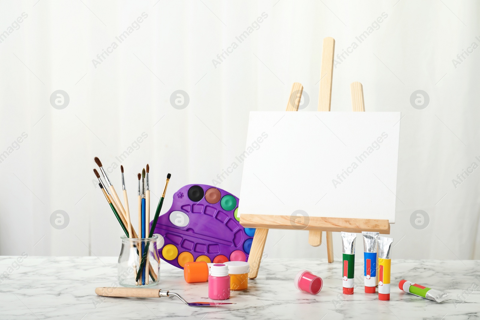 Photo of Wooden easel with blank canvas board and painting tools for children on table in room