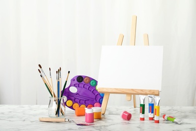 Photo of Wooden easel with blank canvas board and painting tools for children on table in room
