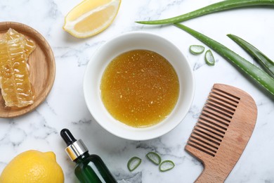 Homemade hair mask in bowl, ingredients and bamboo comb on white marble table, flat lay