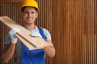 Handsome carpenter wearing uniform near wooden wall. Space for text