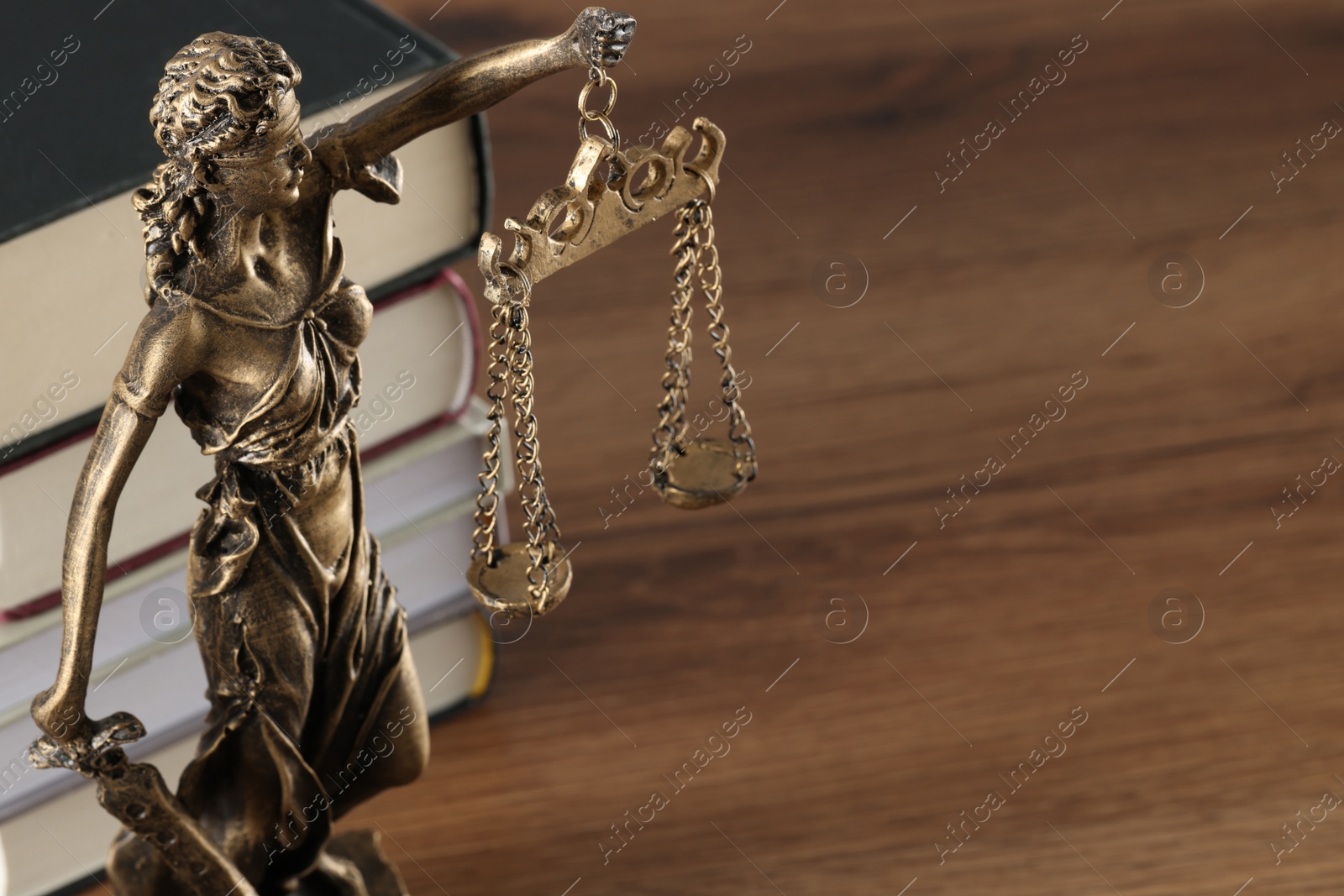 Photo of Symbol of fair treatment under law. Figure of Lady Justice and books on wooden table, closeup with space for text