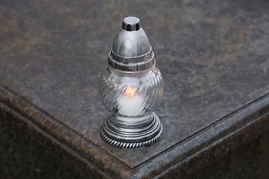 Grave lantern with burning candle on granite surface in cemetery
